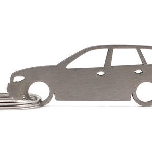 Op de afbeelding: Een zilveren metalen sleutelhanger in de vorm van een auto. De sleutelhanger heeft een sleutelring die aan de onderkant is bevestigd.