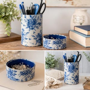 May include: A set of two matching desk organizers, one tall and one short, featuring a blue floral pattern on a white background. The tall organizer holds pens and scissors. The short organizer is filled with paperclips. The organizers are made of a tin material.