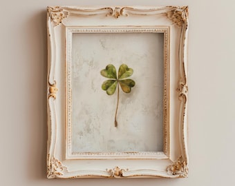 May include: A four-leaf clover pressed and framed in a white ornate frame. The frame has a distressed white finish and gold accents.