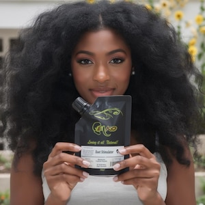 May include: A black pouch of "CEKO Root Stimulator" is held in front of a person. The pouch has a black cap and a green logo. The text "Loving it all Natural!" and "Root Stimulator" are visible. The person has long, dark, curly hair.