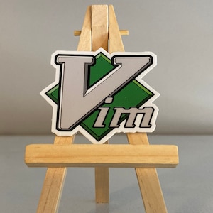May include: A white and green sticker with the text "vim" on a small wooden easel.