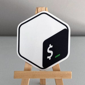 May include: A white and black hexagonal sticker with a dollar sign and an underscore. The sticker is on a small wooden easel.