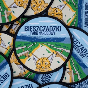 May include: A close-up of several round, blue and white patches with black trim. The patches feature a cartoon lynx and the text "Bieszczadzki Park Narodowy" which translates to "Bieszczady National Park".