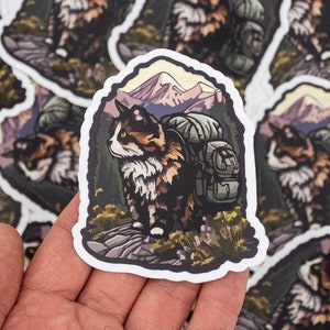 May include: A sticker featuring a cartoon cat wearing a backpack and hiking in the mountains. The cat is brown, white, and black with green eyes. The mountains are purple and pink with a yellow sky. The sticker is on a white background.
