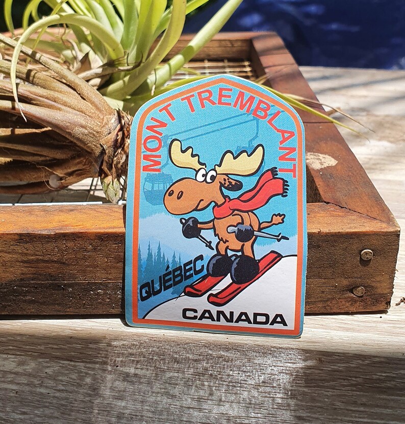 K&ouml;nnte beinhalten: Ein blauer und wei&szlig;er Aufkleber mit einem Cartoon-Elch, der Ski f&auml;hrt. Der Aufkleber zeigt "Mont Tremblant" in einem wei&szlig;en Bogen &uuml;ber dem Elch, "Quebec" in wei&szlig; unter dem Elch und "Canada" in wei&szlig; unten.
