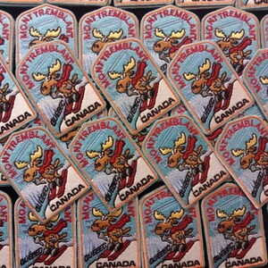 K&ouml;nnte beinhalten: Eine Sammlung bunter gestickter Aufn&auml;her mit einem Cartoon-Elch, der einen Berg hinunterskif&auml;hrt. Jeder Aufn&auml;her tr&auml;gt den Text "Mont Tremblant" und "Quebec, Kanada".