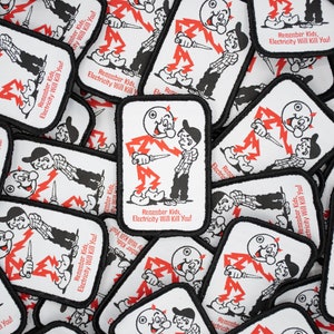 May include: A close-up of a pile of white fabric patches with black borders. Each patch features a cartoon illustration of a stick figure with a lightning bolt and the text "Remember Kids, Electricity Will Kill You!"