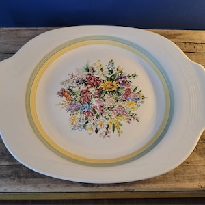 May include: White oval serving platter with a floral design featuring a bouquet of colorful flowers in the center. The platter has a yellow, green, and blue rim.