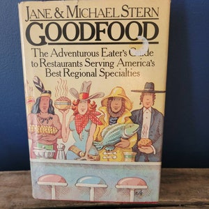 May include: A vintage book cover with a colorful illustration of four people sitting at a counter. The book title is "GOODFOOD: The Adventurous Eater's Guide to Restaurants Serving America's Best Regional Specialties" by Jane & Michael Stern.