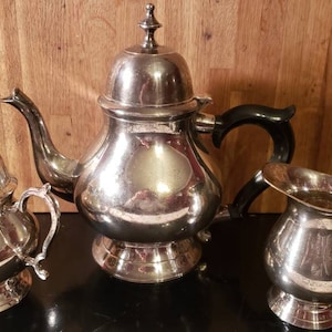 May include: A silver tea set with a teapot, creamer, and sugar bowl. The teapot has a black handle and a shiny, reflective surface.