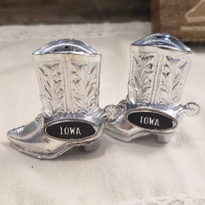 May include: A pair of silver cowboy boot salt and pepper shakers with black labels that read "Iowa".