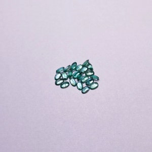 以下が含まれることがあります： 楕円形のターコイズグリーンの宝石のグループ。宝石は白い表面に散らばっています。