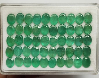 May include: A collection of 40 oval-shaped green gemstones in a clear plastic box. The gemstones are arranged in four rows of ten.