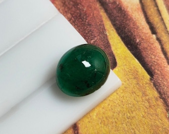 Pode incluir: Uma gema esmeralda cabochão verde-escura com uma superfície lisa e polida.