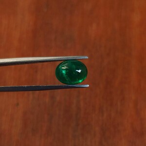 May include: A bright green gemstone held in silver tweezers against a brown wooden background.