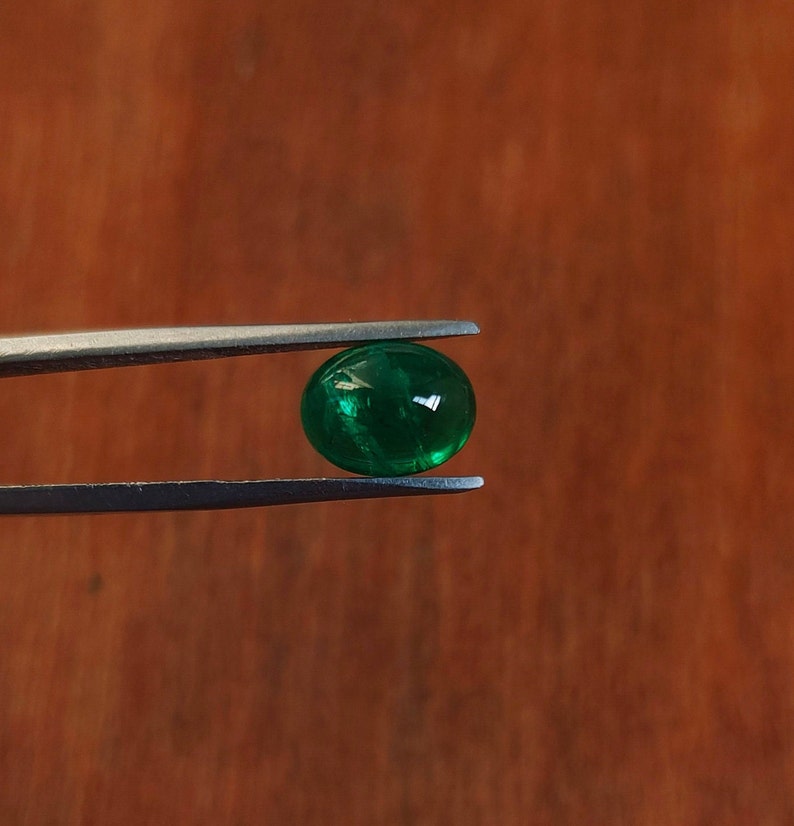 May include: A bright green gemstone held in silver tweezers against a brown wooden background.