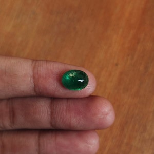 May include: A round, green emerald gemstone with a smooth, polished surface.