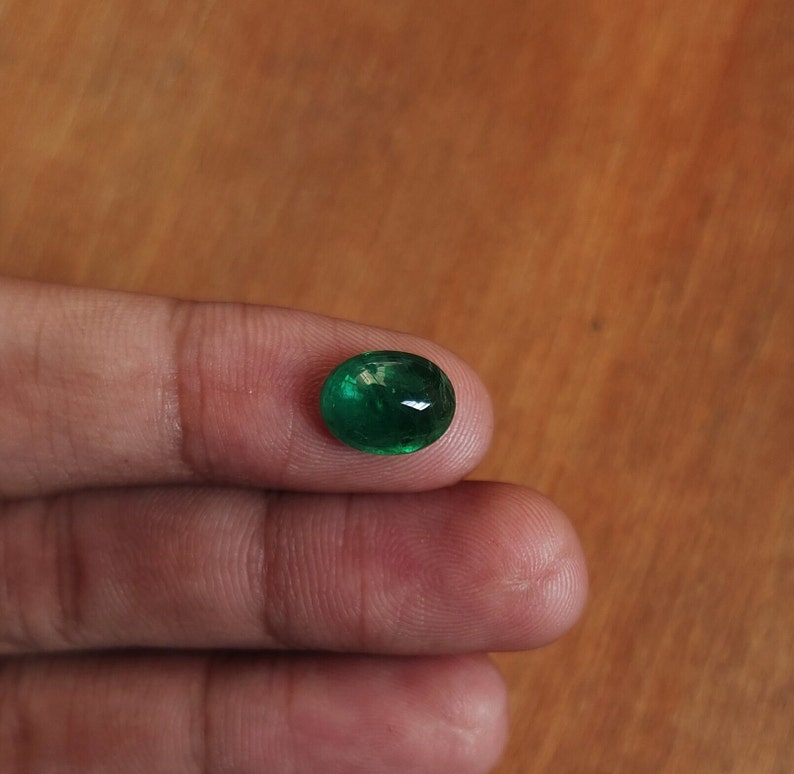 May include: A round, green emerald gemstone with a smooth, polished surface.