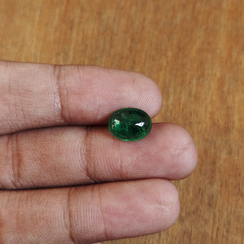 May include: A vibrant green oval-shaped gemstone with a smooth, polished surface.