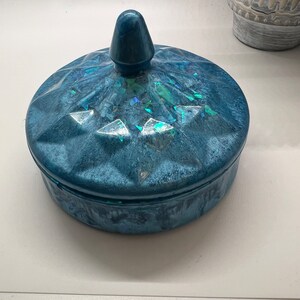May include: A blue ceramic trinket box with a domed lid and a pointed finial. The lid has a iridescent finish and the box has a textured surface.
