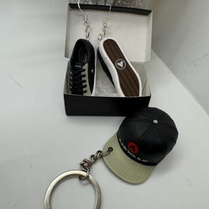 May include: A pair of black and white shoe earrings and a black and white Airwalk keychain with a black baseball cap.