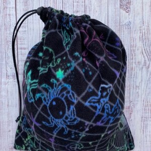 May include: A black drawstring bag with a colorful constellation print. The print features various constellations, including a crab, a fish, and a unicorn.