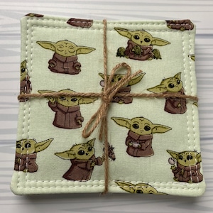 Puede incluir: Conjunto de cuatro posavasos de tela verde con un patr&oacute;n repetido de un personaje de dibujos animados de la franquicia Star Wars. Los posavasos est&aacute;n atados con cuerda.