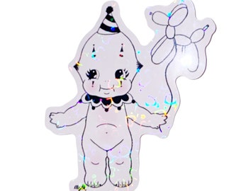 May include: A holographic sticker featuring a cartoon baby wearing a party hat and holding a balloon animal. The baby has a black and white clown costume and a happy expression.