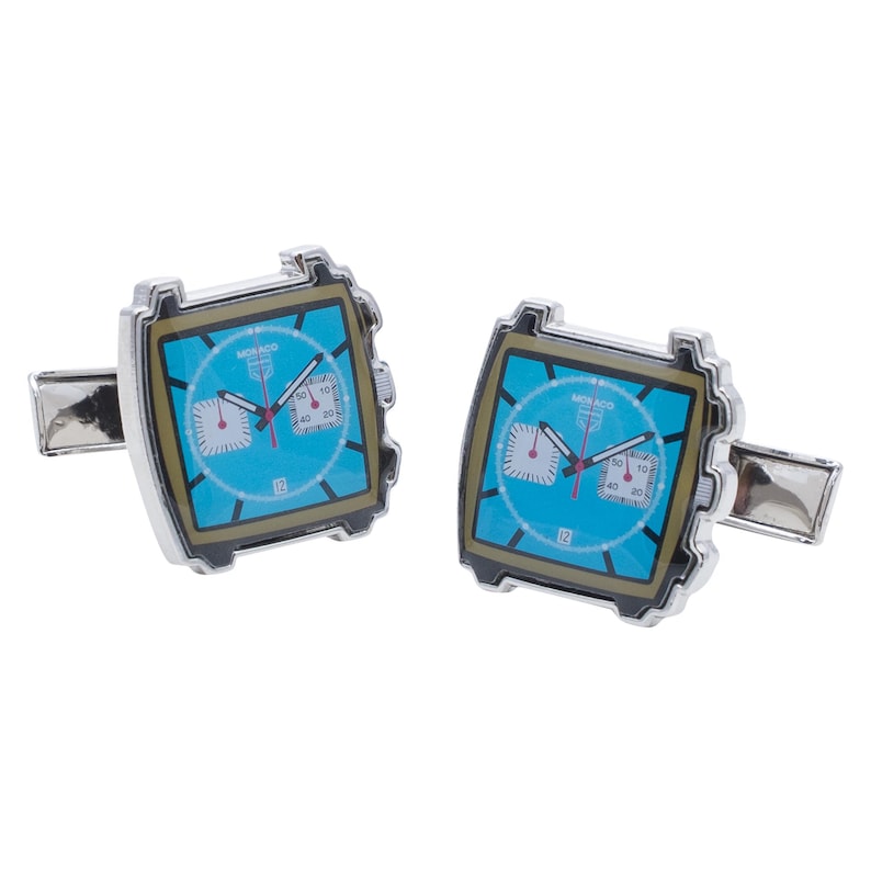 May include: A pair of silver cufflinks with a blue face chronograph watch design. The watch face has the word "Monaco" printed on it.