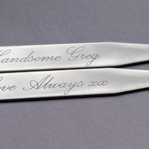 Può includere: Due fermagli per colletto in argento con messaggi incisi. Il fermaglio superiore recita "Handsome Greg". Il fermaglio inferiore recita "Love Always xxx".