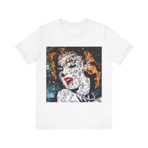 May include: White t-shirt with a colorful graphic print of a woman's face. The graphic is made up of small, colorful squares and the woman's face is stylized.