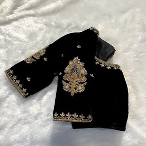 May include: A black velvet blouse with gold and silver embroidery. The blouse has a round neckline and three-quarter sleeves.