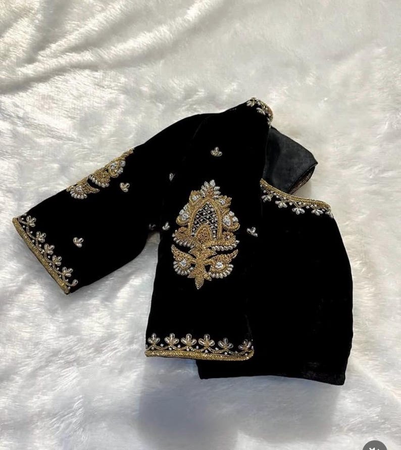 May include: A black velvet blouse with gold and silver embroidery. The blouse has a round neckline and three-quarter sleeves.