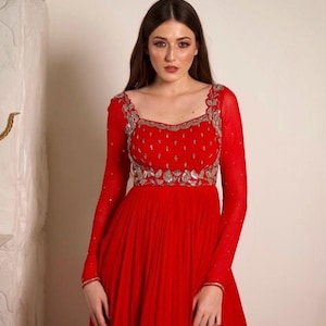 May include: A red floor-length dress with long sleeves and a silver embroidered neckline. The dress has a fitted bodice and a flowing skirt.