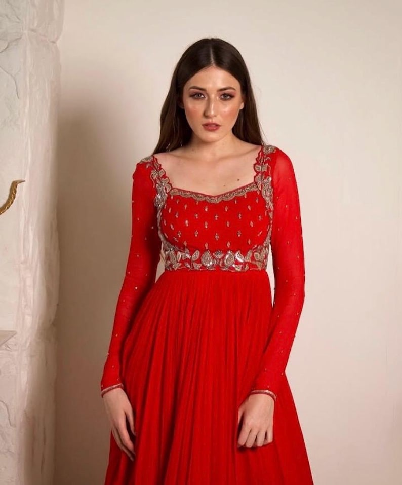 May include: A red floor-length dress with long sleeves and a silver embroidered neckline. The dress has a fitted bodice and a flowing skirt.
