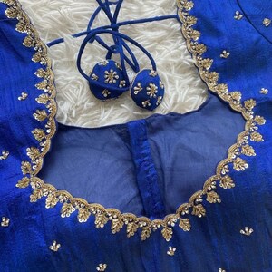 May include: A royal blue fabric with gold and silver embroidery. The fabric has a scalloped edge and is decorated with small, round sequins. The fabric is likely for a garment, such as a blouse or dress.