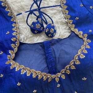 May include: A royal blue fabric with gold and silver embroidery. The fabric has a scalloped edge and is decorated with small, round sequins. The fabric is likely for a garment, such as a blouse or dress.
