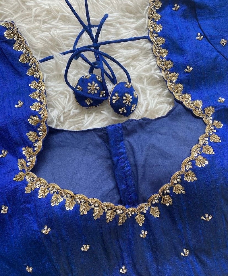 May include: A royal blue fabric with gold and silver embroidery. The fabric has a scalloped edge and is decorated with small, round sequins. The fabric is likely for a garment, such as a blouse or dress.