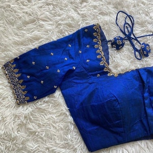 May include: A royal blue silk blouse with gold embroidery and a scalloped edge. The blouse has a tie closure at the back.