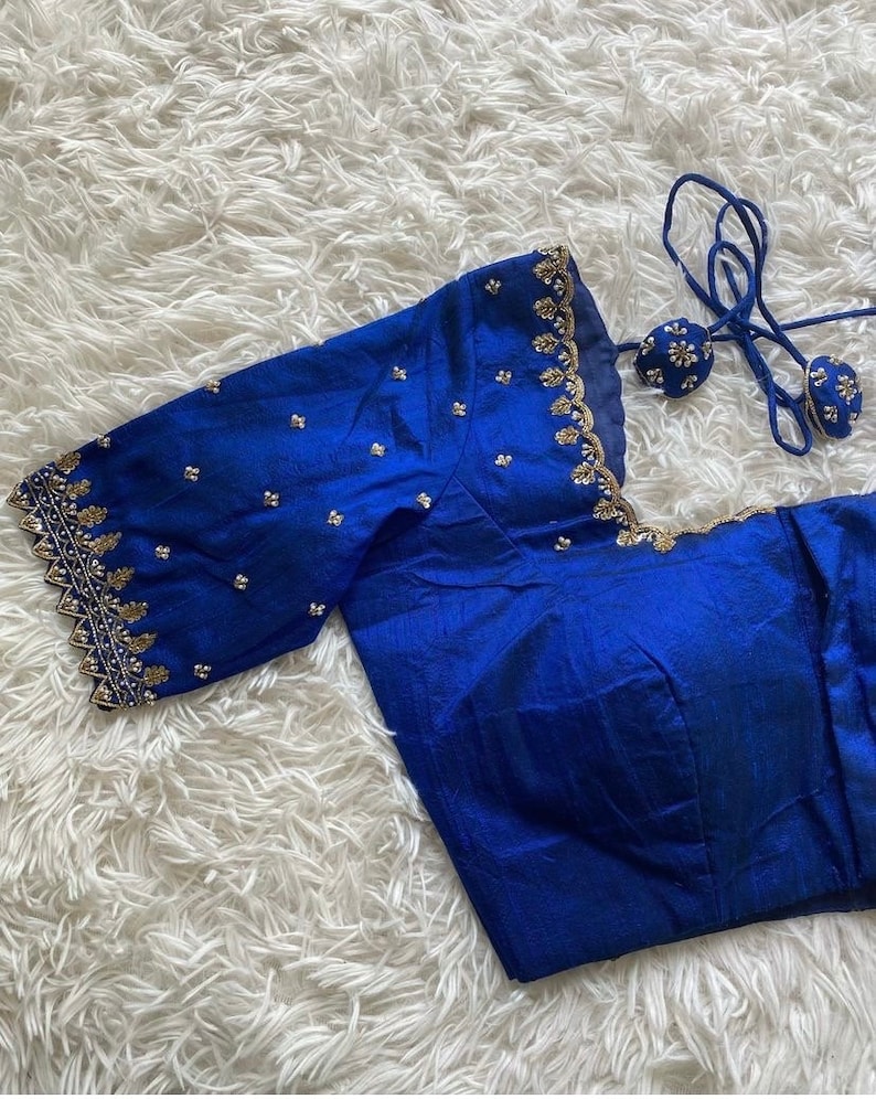 May include: A royal blue silk blouse with gold embroidery and a scalloped edge. The blouse has a tie closure at the back.