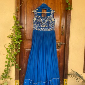 May include: A royal blue floor-length dress with gold embroidery and a white trim. The dress has a sleeveless design and a scoop neckline.