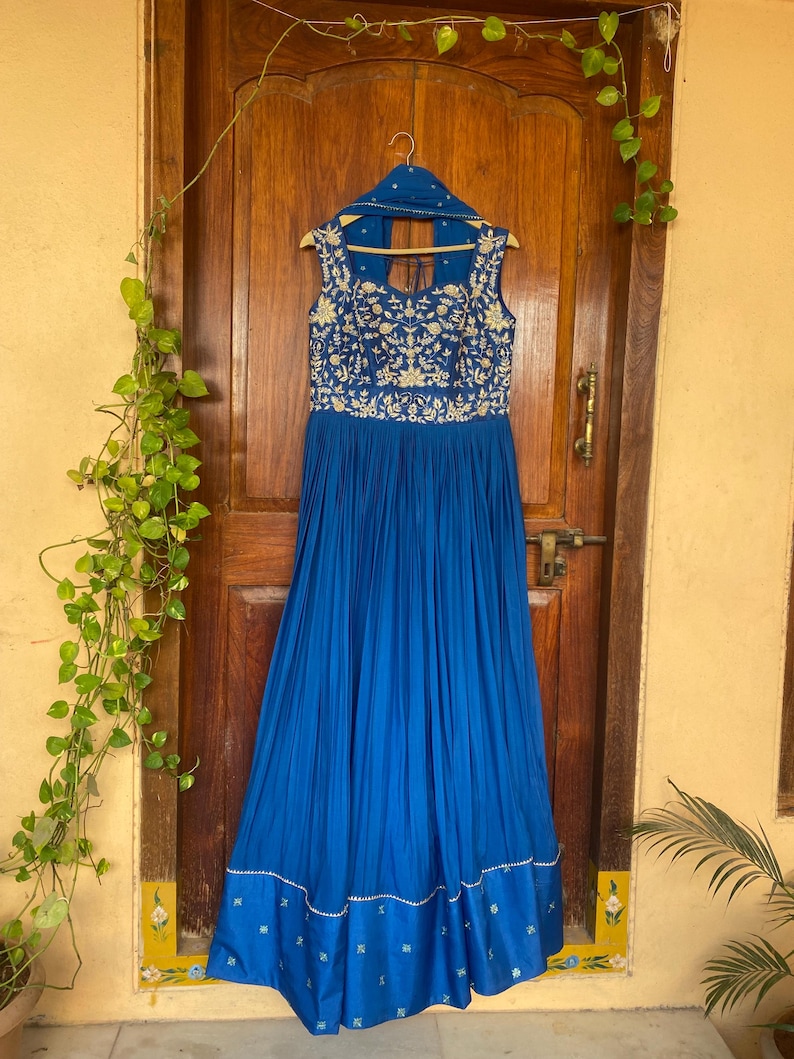 May include: A royal blue floor-length dress with gold embroidery and a white trim. The dress has a sleeveless design and a scoop neckline.