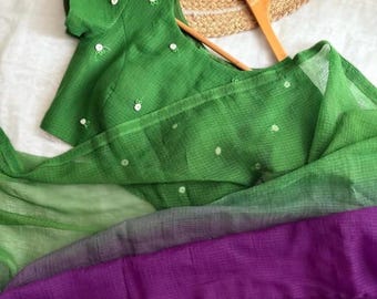 May include: A green and purple ombre saree with white embroidered dots. The saree is draped over a wooden hanger.