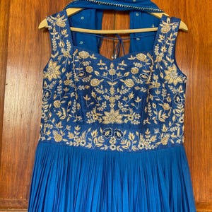 May include: A blue sleeveless dress with gold embroidery and a matching blue scarf. The dress has a pleated skirt and a sweetheart neckline.