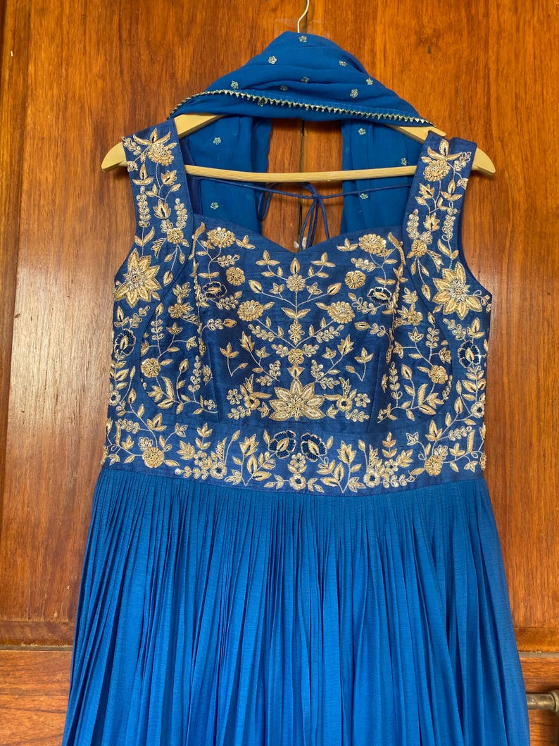 May include: A blue sleeveless dress with gold embroidery and a matching blue scarf. The dress has a pleated skirt and a sweetheart neckline.