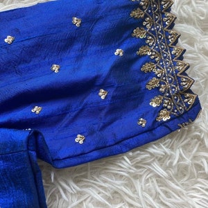 May include: A royal blue fabric with a gold and white embroidered trim. The fabric is decorated with small, silver sequins.