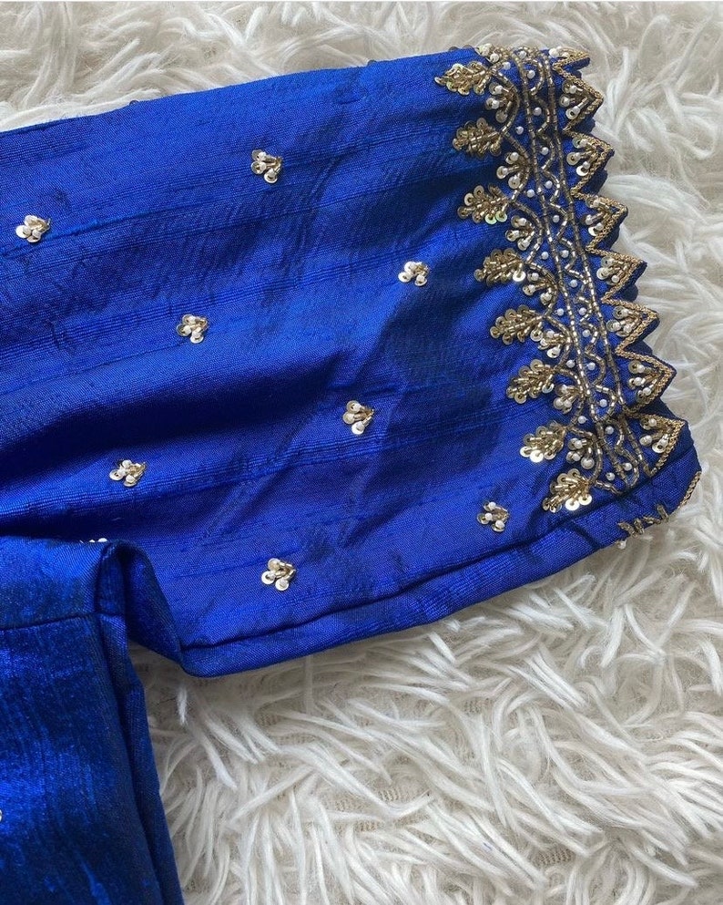 May include: A royal blue fabric with a gold and white embroidered trim. The fabric is decorated with small, silver sequins.
