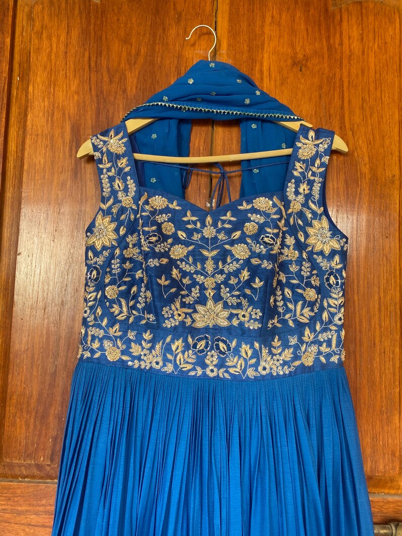 May include: A blue sleeveless dress with gold embroidery and a matching blue scarf. The dress has a pleated skirt and a sweetheart neckline.