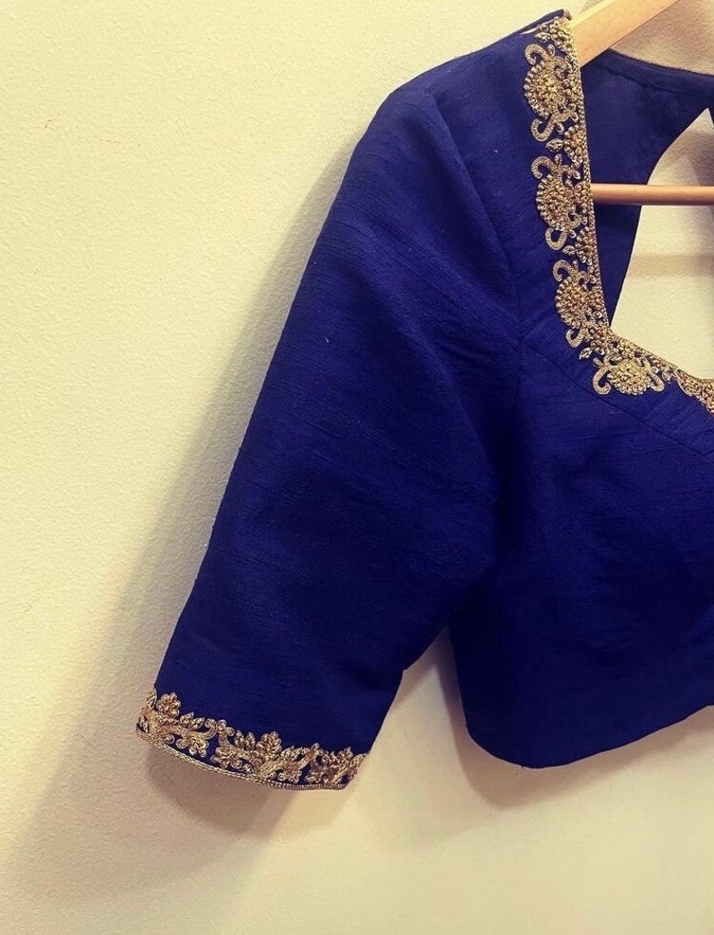 Op de afbeelding: Een donkerblauwe blouse met gouden borduurwerk rond de halslijn en mouwen. De blouse is gemaakt van een zachte, zijdeachtige stof.