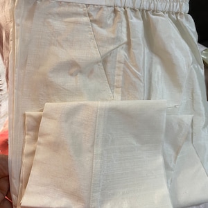 May include: White cotton pants with a drawstring waistband and a folded cuff. The pants are made of a lightweight fabric and have a subtle sheen.